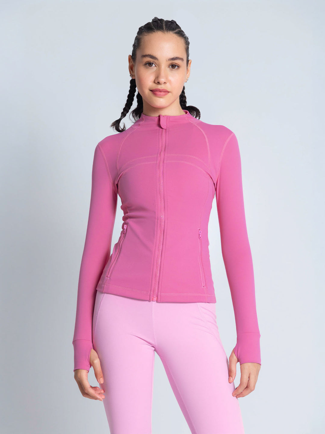 A woman modeling a bright pink long-sleeve athletic zip-up jacket and matching pink leggings against a light gray studio background. pink workout jacket. lululemon define jacket