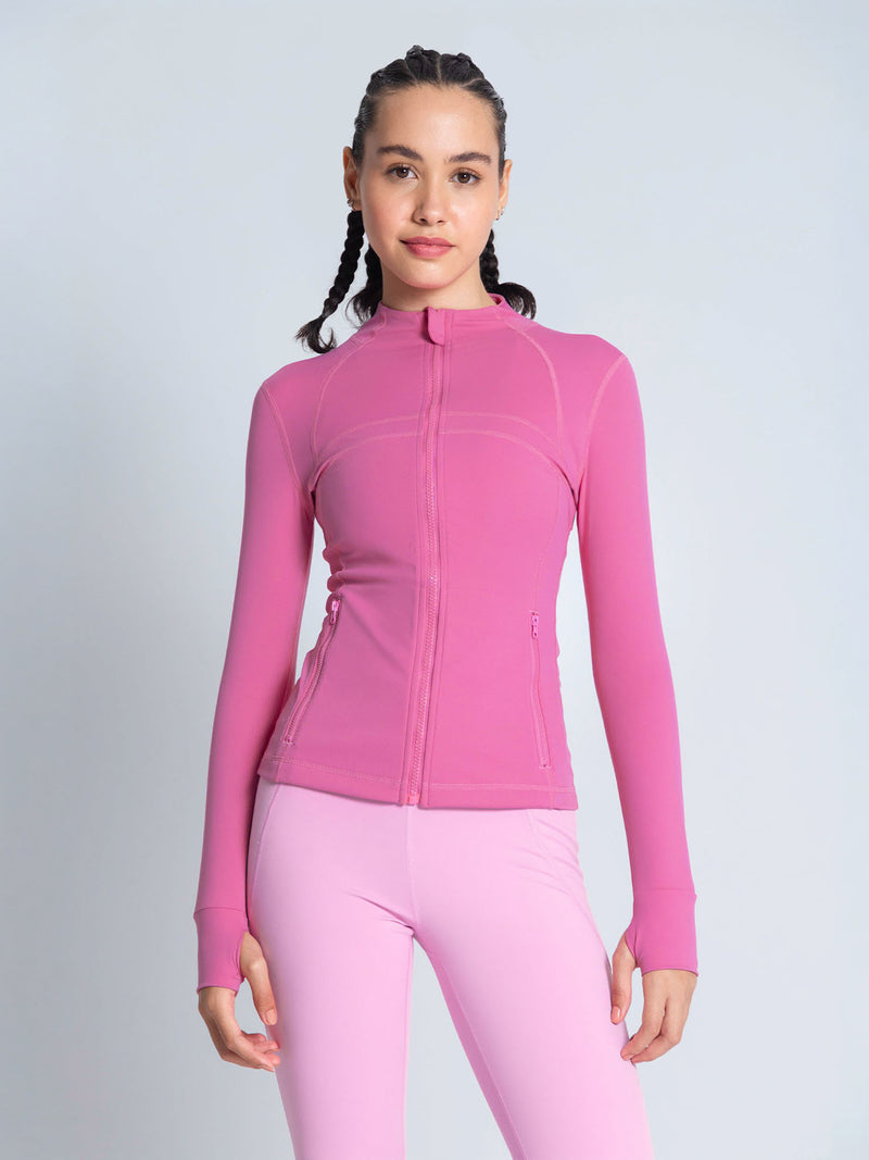 A woman modeling a bright pink long-sleeve athletic zip-up jacket and matching pink leggings against a light gray studio background. pink workout jacket. lululemon define jacket
